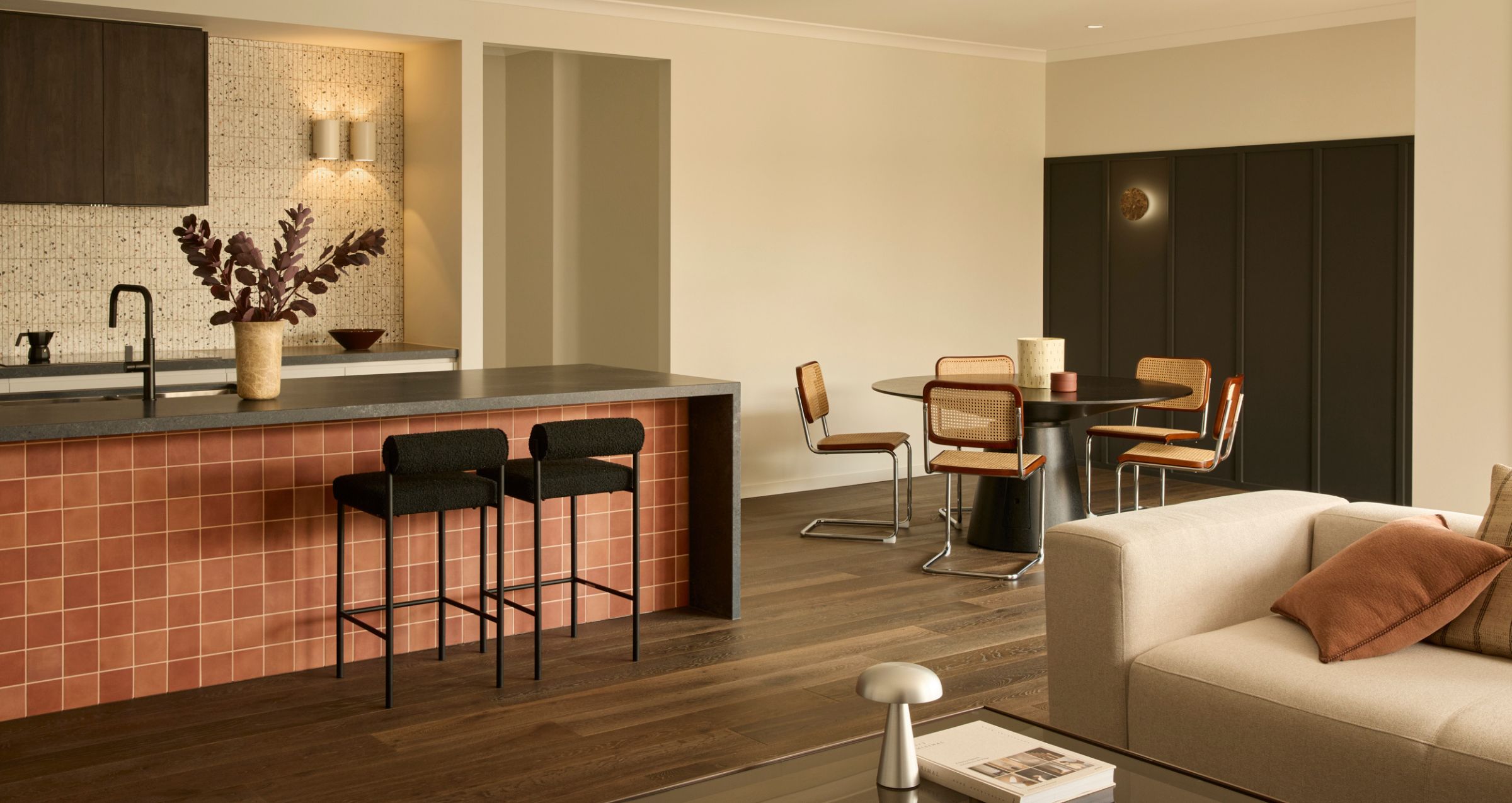 Boutique Homes open-plan kitchen, dining and living space featuring a tiled island bench, timber flooring and a warm, cohesive material palette.