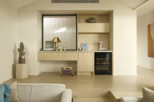 Coastal-inspired living room joinery with light oak cabinetry, built-in shelving, wine fridge and layered styling in the Cottage by the Sea Charity Home, designed for warm, relaxed family living.